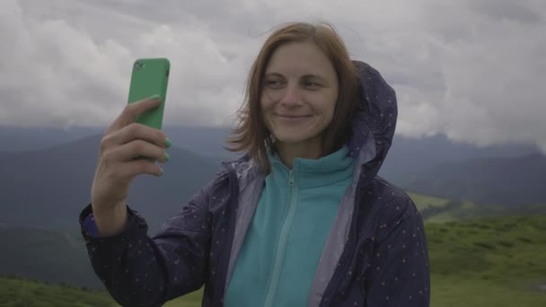 30 γυναίκα ταξιδιώτη λήψη selfie εικόνα στο κινητό τηλέφωνο στέκεται σε συννεφιά βουνά. Λήψη φωτογραφιών του τοπίου. — Αρχείο Βίντεο