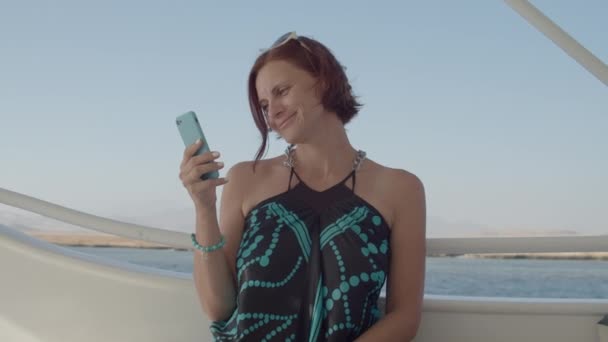 30 років жінка в одязі, використовуючи мобільний телефон, що пливе на човні в морі. Усміхнена жінка на кораблі . — стокове відео