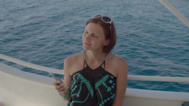 Młoda, dorosła kobieta pływająca na łodzi i ciesząca się morzem. Osoba zabiera telefon komórkowy na relaks z widokiem na morze. — Wideo stockowe