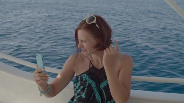 Dertiger jaren vrouw in jurk praten op video conferentie zeilen op zee boot met behulp van een smartphone. Vrouwelijk chatten op video gesprek met mobiele telefoon in handen zittend op jacht. — Stockvideo