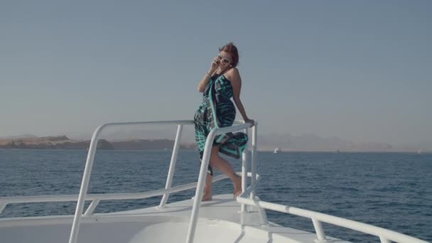 Молода доросла жінка в одязі розмовляє мобільним телефоном, що стоїть на яхті. Жінка розмовляє за допомогою клітини, що пливе на морському човні . — стокове відео