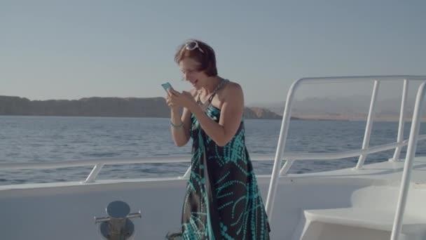 Mujer de 30 años en vestido leyendo buenas noticias en el teléfono móvil y conseguir muy exitado al respecto navegando en barco en el mar. Mujer muy feliz saltando leyendo buenas noticias en la celda. — Vídeos de Stock
