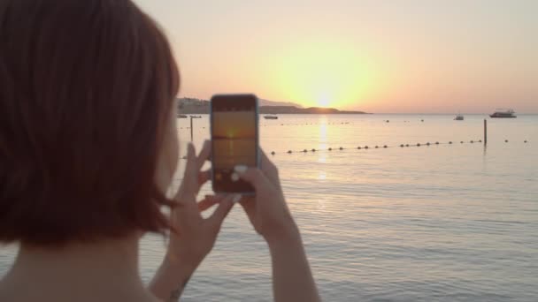 Frau fotografiert Sonnenaufgang über dem Meer mit dem Handy. Früh morgens am Meer. Genießen Sie die Morgendämmerung über den Bergen. Weibchen nimmt Foto-Erinnerungen auf Handy auf. — Stockvideo