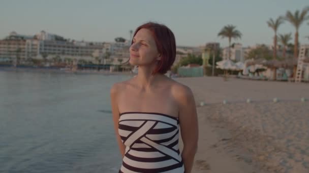 Een vrouw uit de 30 in een badpak die over de kust loopt en de prachtige zonsopgang boven de zee ziet. Vrouw geniet van de dageraad op het strand. — Stockvideo