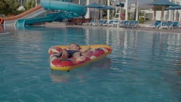 Çocuk yüzme havuzunda şişme pizzanın üzerinde yatıyor. Kaygısız çocuk havuzda yalnız.. — Stok video