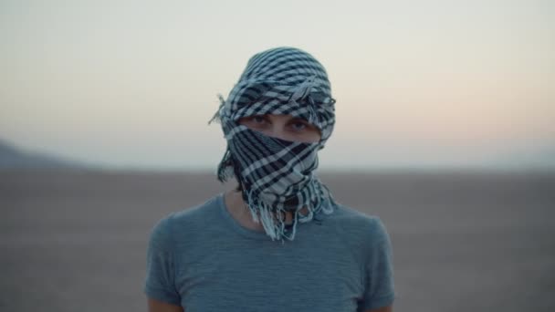 Portret van een vrouw met een geruite keffiyeh die in de woestijn staat en naar de camera kijkt. Blanke vrouwelijke toerist in de woestijn. — Stockvideo