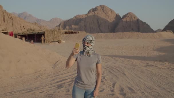 Toerist in geruite keffiyeh op zoek naar mobiele netwerk met behulp van mobiele telefoon staan in de woestijn. Vrouw op zoek naar mobiel signaal in de woestijn. Geen signaal van de exploitant. — Stockvideo