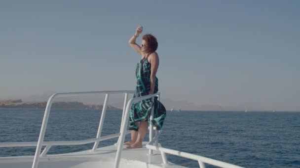 Kobieta 30s w sukience cieszy się widokiem na morze żeglarstwo na łodzi. Szczęśliwa zrelaksowana kobieta stojąca na nosie jachtu patrząca w kamerę. — Wideo stockowe