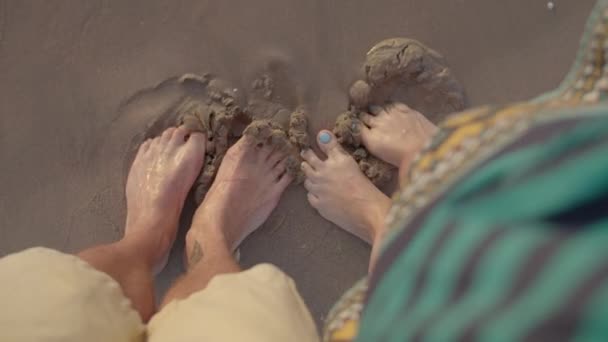 남편 과 아내는 맨 발로 해변에서 모래를 가지고 놀고 있다. 파도는 부부 의발을 씻어 준다. 사람의 다리의 맨 위 모습. — 비디오