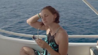 Beyaz yatta yelken açan 30 'lu yaşlarda güneş gözlüklü bir kadın. Güneş gözlüklü bir kadın denizde yelken açmaktan hoşlanıyor..