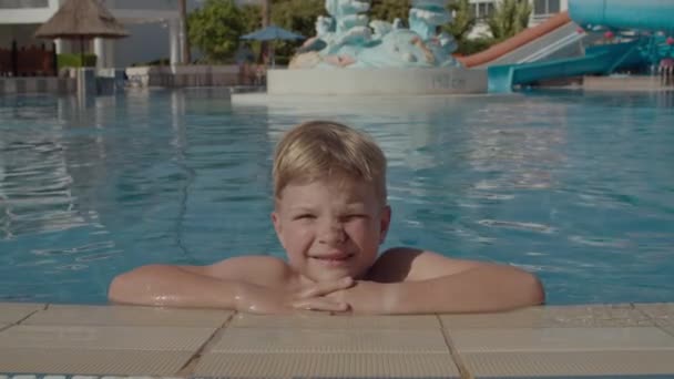 Havuzda gülümseyen ve kameraya bakan sarışın çocuğun portresi. 6 yaşında bir çocuk havuzda yüzüyor. Yaz neşesi. — Stok video