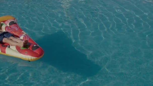 6 éves fiú zenét hallgat és felfújható pizzán pihen a medencében. Gondtalan nyári szabadidő a medencében. — Stock videók