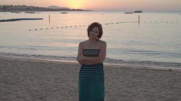 Dertiger jaren vrouw in jurk, staande op het strand bij zonsopgang boven de zee. Vroeg in de ochtend aan de kust. — Stockvideo