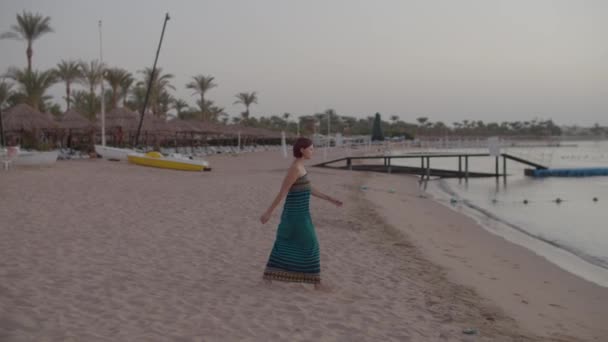 Adult woman in dress walking barefoot to the sea early in the morning. Empty beach. — Stock Video