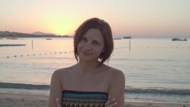 Retrato de mujer de 30 años vestida de pie en la playa al amanecer sobre el mar. Por la mañana temprano en la orilla del mar. — Vídeo de stock