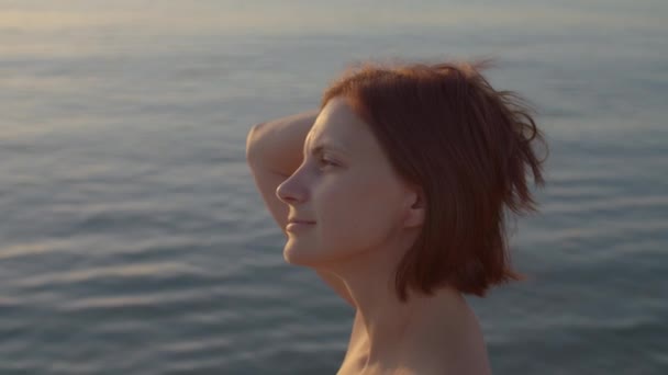 Mujer de 30 años pensativa de pie junto al mar y disfrutar del tiempo a solas. Temprano en la orilla del mar. Mar sol alegría. — Vídeo de stock