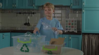 Gönüllü mavi tişörtlü çocuk kağıt ve plastik şişeleri yeşil geri dönüşüm işaretli kaplara ayırıyor. Ev geri dönüşüm süreci. Geri dönüşümü kolay.