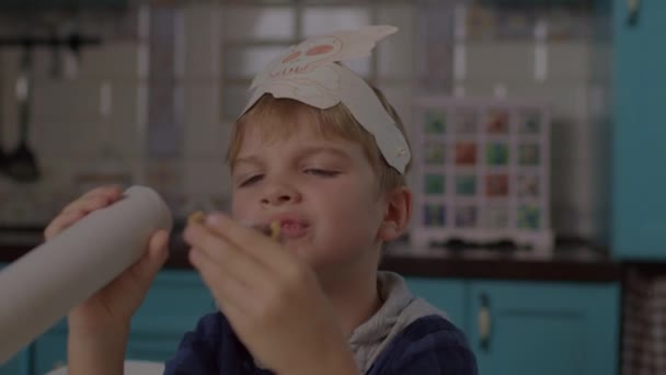 Kid äter godis medan du spelar pirater spel med pappersteleskop och huvudbonader med skalle och skelett. Förskola pojke i pirater hatt ler mot kameran. — Stockvideo