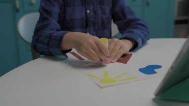 6 yaşındaki çocuk evde sanat yapıyor. Çocuk yapıştırıcı ve makasla renkli kağıt resmi yapıyor. Çocukların yaratıcılığı.