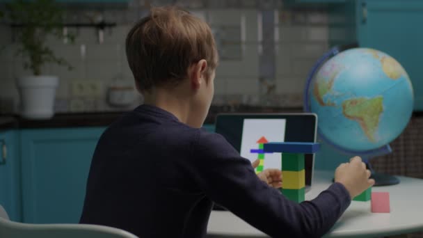 Autistic boy building con bloques de madera de color usando tableta de computadora. Asignación en línea a un alumno con autismo. Análisis de comportamiento aplicado para estudiantes con autismo. Sobre la vista del hombro. — Vídeos de Stock