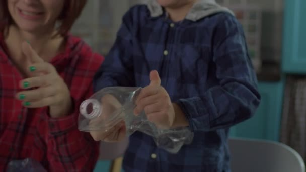 Près de 30 ans mère et fils triant les déchets recyclables à la maison. Tri familial du papier, du verre et des matières plastiques recyclables dans des conteneurs avec panneau de recyclage vert. — Video