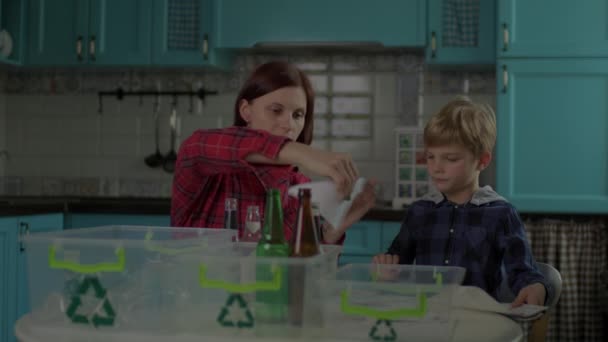 30 μητέρα και γιος διαλογή ανακυκλώνουν τα απόβλητα στο σπίτι. Οικογενειακό χαρτί διαλογής, ανακυκλώσιμα υλικά από γυαλί και πλαστικό σε δοχεία με πράσινη πινακίδα ανακύκλωσης. — Αρχείο Βίντεο