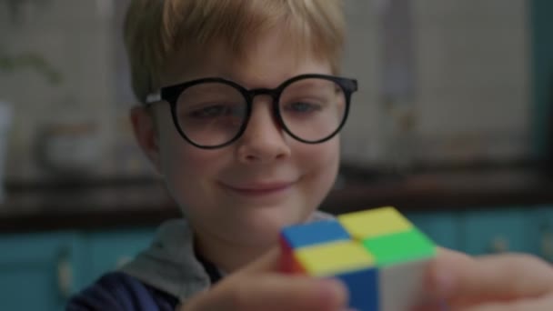 Close up de menino em óculos de olho resolvendo quebra-cabeça cubo de cor nas mãos. Criança inteligente brincando com quebra-cabeças cubo. — Vídeo de Stock