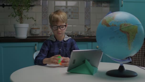 Niño de 6 años de edad en gafas de ojo resolver rompecabezas cubo de color en las manos. Niño jugando con rompecabezas cubo inteligente. Niño confundido debido a rompecabezas duro. — Vídeos de Stock