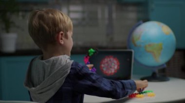 Okullu çocuk evde oturup renkli yapboz oyuncakları oynuyor ve virüs modeli yapıyor. Virüsü oyuncaklarla modellemek için tablet bilgisayar kullanan çocuk.