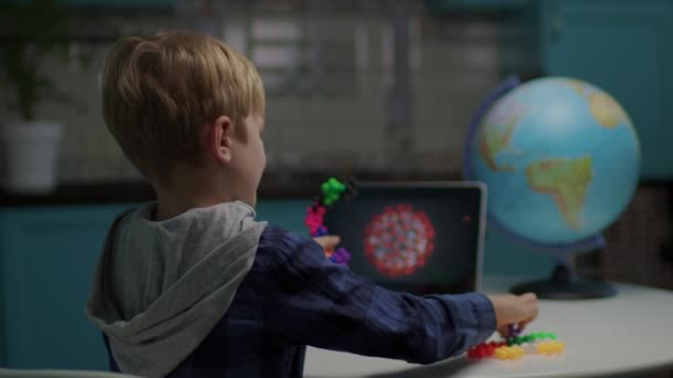 Back of school boy playing color puzzle toys making model of virus sitting at home. Dítě používající tablet pro modelování viru s hračkami. — Stock video
