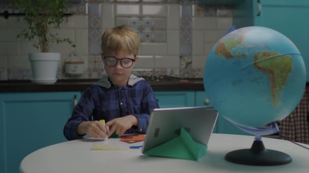 School boy making applique with color paper and glue looking at tablet computer. Kids creativity at home. Online art class. — Stock Video