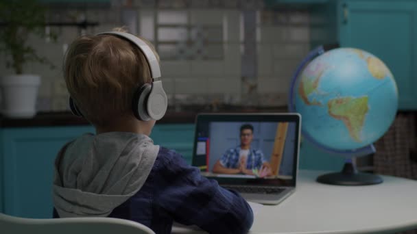 Szkolny chłopiec uczący się online przy użyciu laptopa z Afroamerykańskim nauczycielem na ekranie komputera. Dzieciak w słuchawkach ma zajęcia online z nauczycielem rozmawiającym przez komputer. Proces kształcenia w domu. — Wideo stockowe