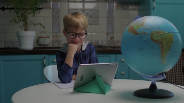 Chico sonriente de la escuela con anteojos mostrando el pulgar hacia arriba mirando la tableta. Educación en línea desde el concepto del hogar. Kid disfruta del aprendizaje a distancia. — Vídeo de stock