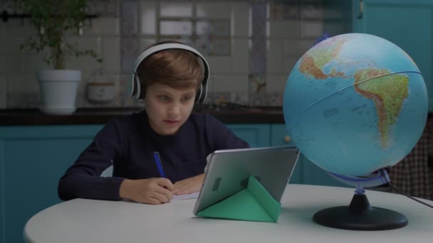 自闭症学童带着耳机，在家里用平板电脑上网学习写字。微笑着从家里学习的自闭症学童. — 图库视频影像