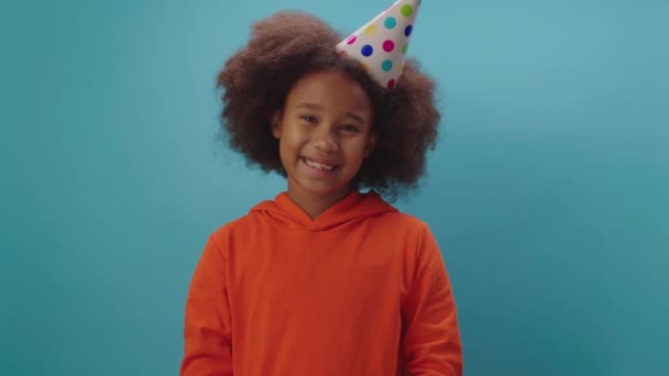 Sorrindo menina afro-americana recebe presente de aniversário de pé no fundo azul. Kid está feliz em receber presente de aniversário. — Vídeo de Stock
