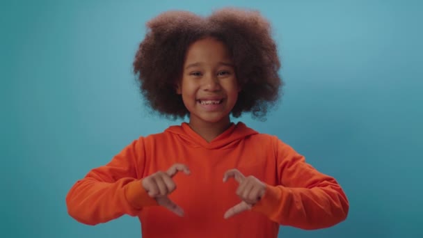 Sonriente chica afroamericana haciendo forma de corazón con los dedos mirando a la cámara. Niño encantador sosteniendo símbolo del corazón de la mano. — Vídeo de stock