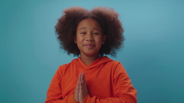 Menina da escola afro-americana implorando em pé sobre fundo azul. Miúdo de mãos dadas a implorar por algo a olhar para a câmara. Criança pedindo por favor falando com a câmera. — Vídeo de Stock