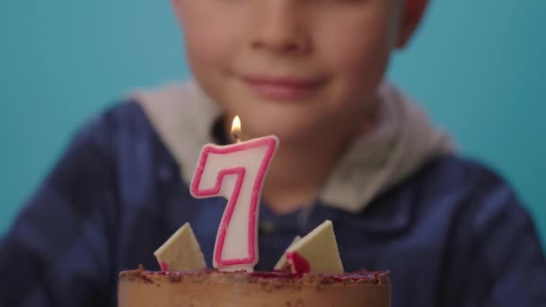 スローモーションで7番のキャンドルを吹いている子供の終わり。7歳の少年は誕生日を祝い、カメラで微笑む。幸せな7歳. — ストック動画