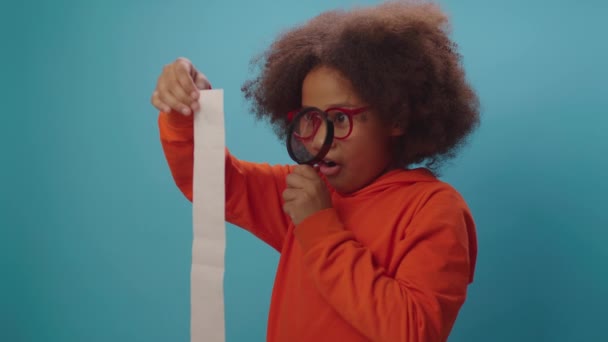 Afro-Amerikaanse jongen kijkt naar een groot bonnetje met vergrootglas. Kind toont wow emotie over grote home budget. — Stockvideo