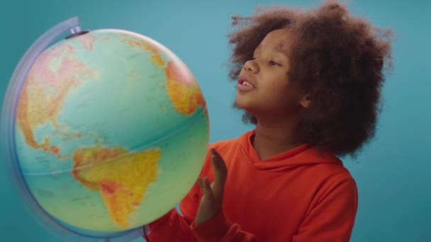 Linda chica de la escuela afroamericana estudiando el mundo y sonriendo a la cámara. Feliz aprendizaje geográfico. — Vídeo de stock