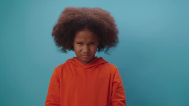 Menina afro-americana mostra emoção irritada em pé sobre fundo azul. O miúdo discorda de algo.. — Vídeo de Stock