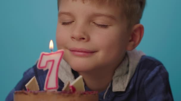 少年を閉じて願い事をし、スローモーションで7番のろうそくを吹き消します。7歳の少年は誕生日を祝う。幸せな7歳の子供. — ストック動画