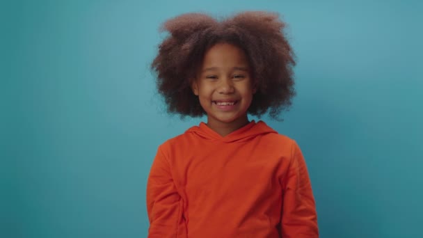 African American girl eating apple standing on blue background. Smiling kid enjoys eating healthy food. — Stock Video