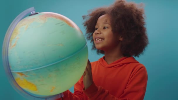Chica de la escuela bastante afroamericana con globo sonriendo a la cámara de pie sobre fondo azul. Geografía de aprendizaje infantil. — Vídeos de Stock