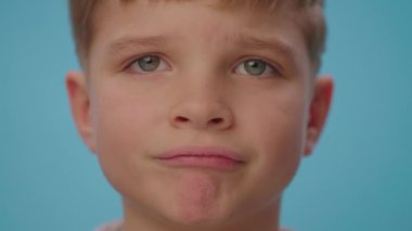 Mavi arka planda hayal kırıklığı gösteren üzgün çocuğa yaklaş. Mutsuz çocuk dudaklarını buruşturuyor..