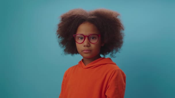 Ładna czarna dziewczyna zmęczona noszeniem okularów i pocieraniem oczami stojącymi na niebieskim tle. Dzieciak z zaburzeniami wzroku w goglach. — Wideo stockowe