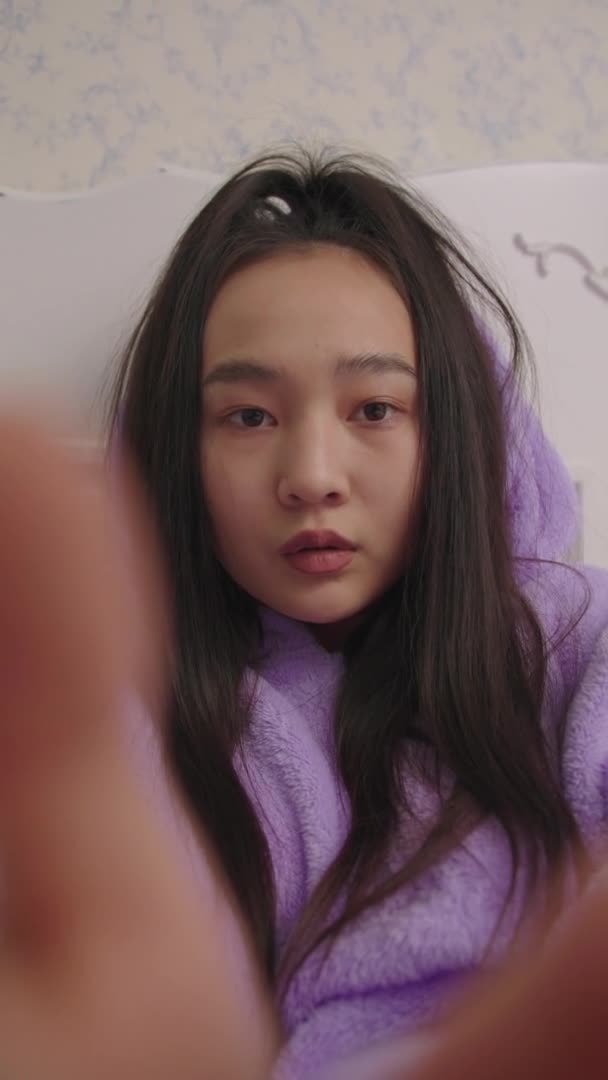 Függőleges videó mobiltelefon POV 20-as ázsiai nő gépelés üzenet fekszik az ágyban. Lila pizsamás nő mobiltelefonnal. — Stock videók