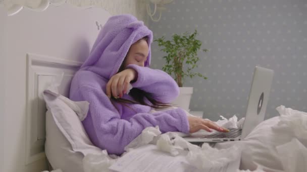 Sick 20s Asian woman working from home, coughing and blowing her nose with napkins lying in bed. Working woman in purple pajamas tired of being ill. — Video Stock