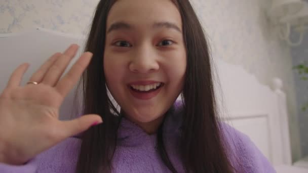 Telefon kamera POV boldog 20-as ázsiai nő beszél videohívás nézi kamera. Csinos nő lila pizsamában beszél a kamera előtt az ágyban.. — Stock videók