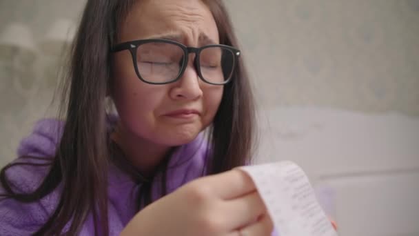 Засмучена молода азіатка в окулярах дивиться на велику квитанцію в магазині. Спантеличені тисячолітнім сімейним бюджетом жінок.. — стокове відео